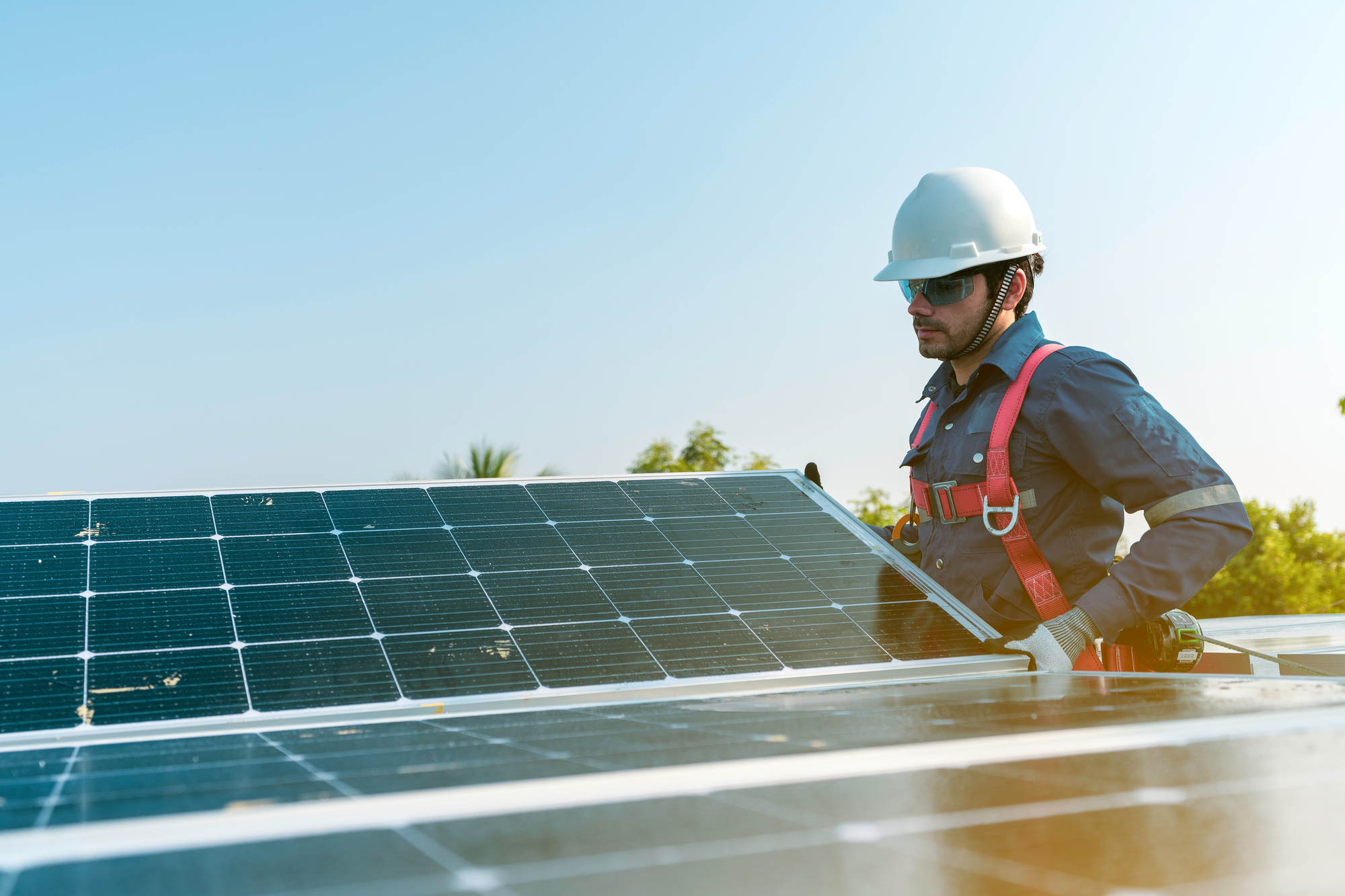 A Person In A Hard Hat And Overalls Standing Next To Solar Panels
